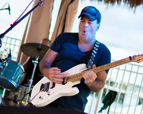 A guitarist singing into a microphone while performing on the covered waterfront deck at On the Edge Bar & Grill