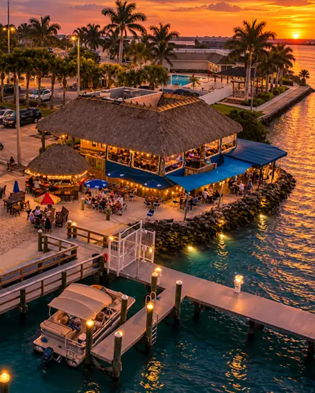 On the Edge Bar & Grill lit up at sunset on the Fort Pierce Inlet, diners on the thatched-roof deck and boats tied up at the dock